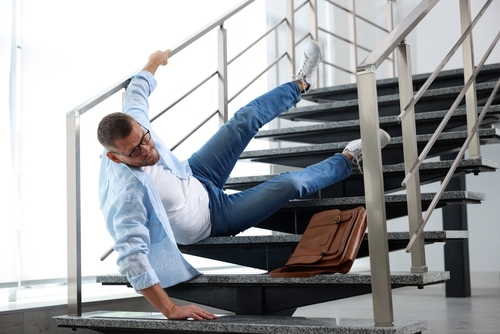 Man falling backward on outdoor building stairs while carrying briefcase and documents