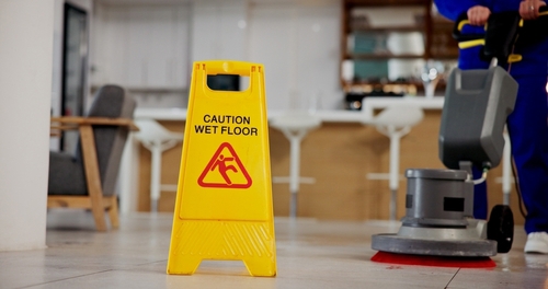 Cleaning worker mopping floor beside caution wet floor sign and cleaning cart