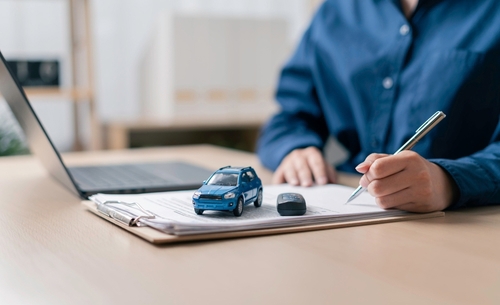 Buyer signing vehicle registration papers with car key and clipboard on desk
